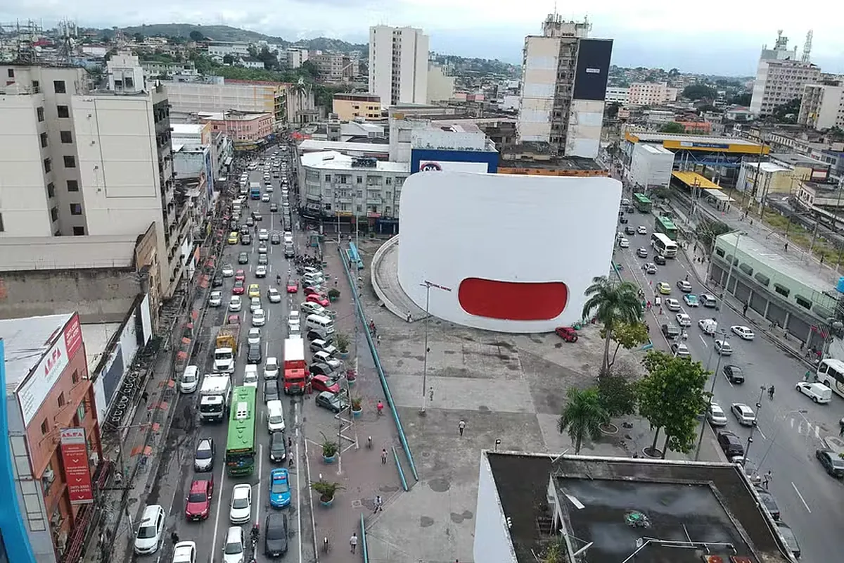 Vista aérea do centro de Duque de Caxias, com a avenida movimentada e o prédio de fachada branca curva