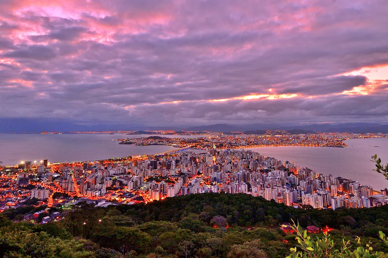 Vista de Florianópolis ao anoitecer, com o centro iluminado, a baía e o continente ao fundo