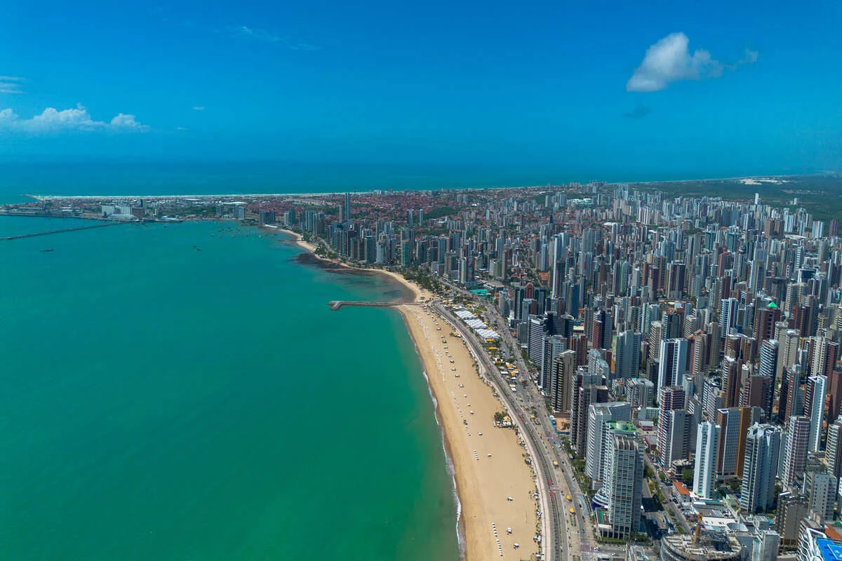 Orla de Fortaleza vista do alto, com a faixa de areia, o mar verde e os edifícios da Beira Mar