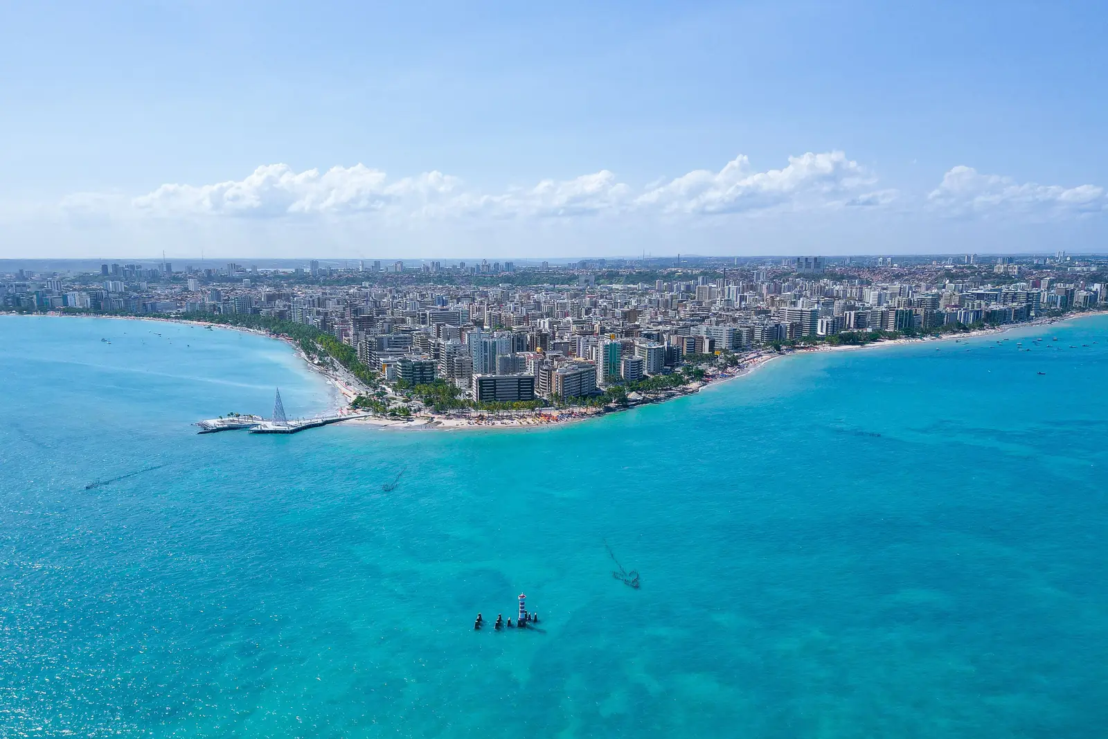 Orla da Pajuçara em Maceió vista do alto, com o mar azul-turquesa, as piscinas naturais e os prédios da orla